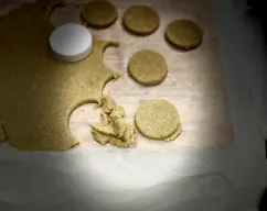 Step <p>Retire la masa del vaso , póngala entre dos laminas de papel de hornear y estríelas con un rodillo, dejando 1 cm de espesor.Deles forma con un corta pastas o haciendo montoncitos con las manos </p><p><br></p> illustration